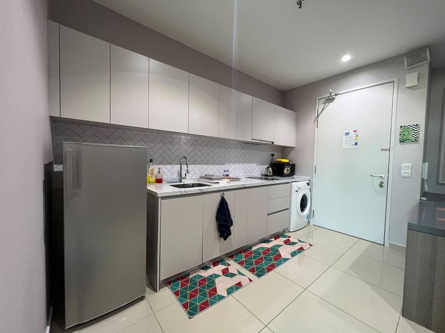 Galley kitchen with overhead cabinets, hob, sink and a washing machine at the far end.